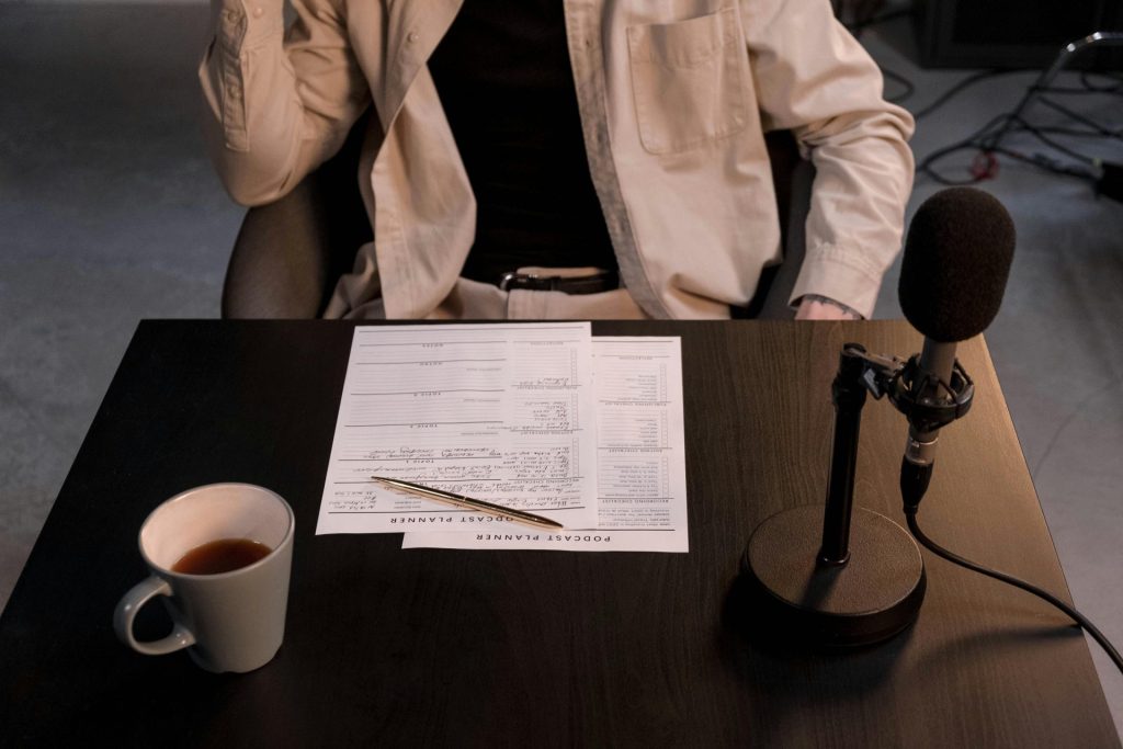 A podcast setup with microphone, papers, and coffee cup on a desk.